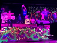 student holding one leg up on stage surrounded by students dancing 